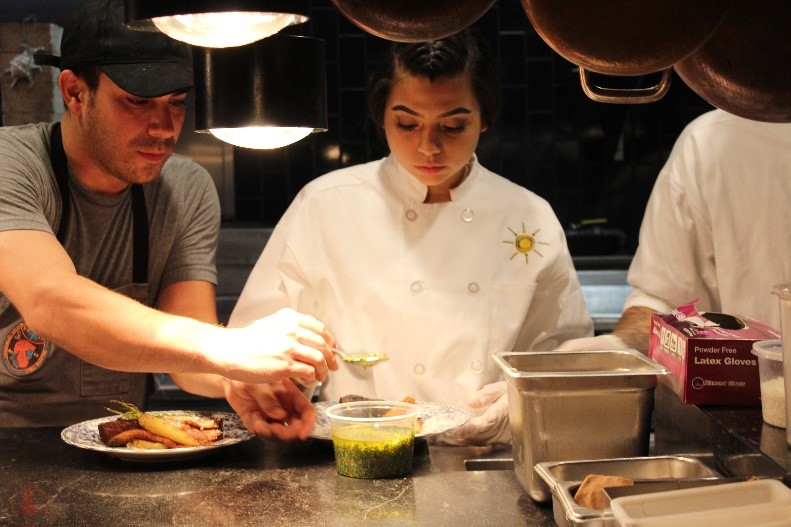 A chef from the Michelin-rated restaurant Rossoblu advises a youth on the
 proper technique for plating a main dish. 