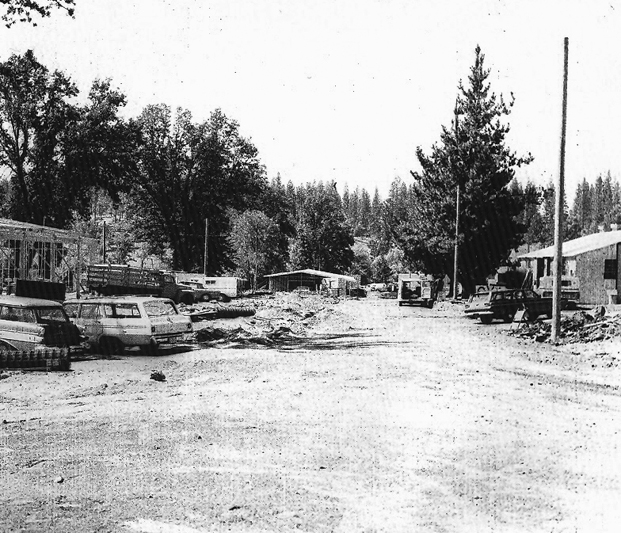 Dirt road with vehicles on the left side and some old buildings.