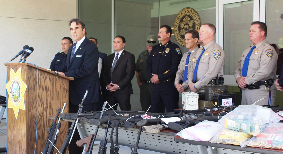 District attorney, law agents stand with seized weapons.