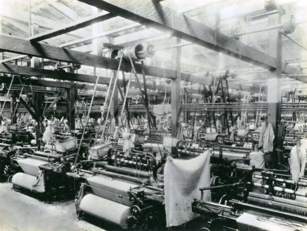 Incarcerated prison workers on the job at the San Quentin State Prison Jute Mill in early 1900s. Looms and cotton textiles fill the room.