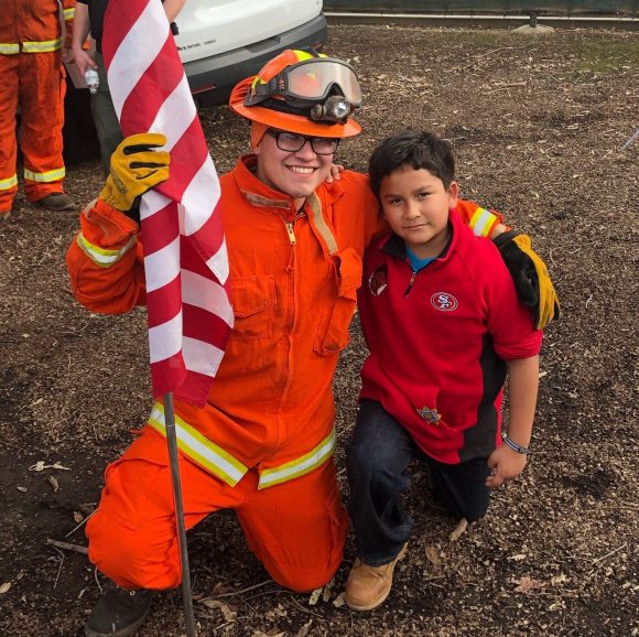 Youth crew member with a child at the Kids Safety Fair at the 2019 Pig Bowl Guns and Hoses charity football game.