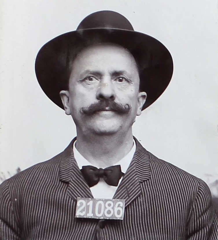 Mustachioed man wearing hat and number 21086.