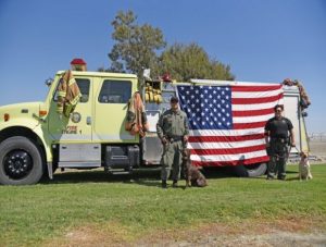 Two officers with police dogs stand in front of a flag.