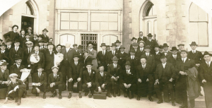 Men in suits stand in front of brick walls.