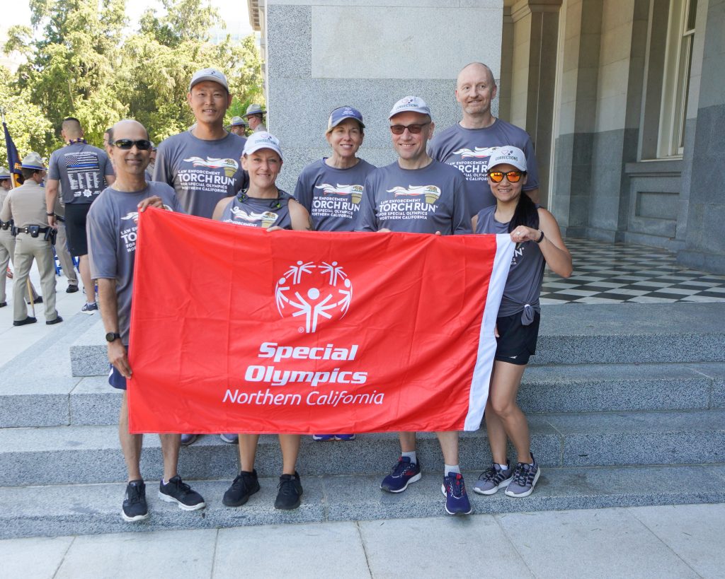 Seven people in matching "Torch Run" shirts hold a red banner that says Special Olympics Northern California.