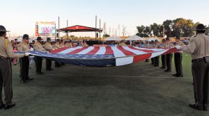 People in uniform hold a large American flag.