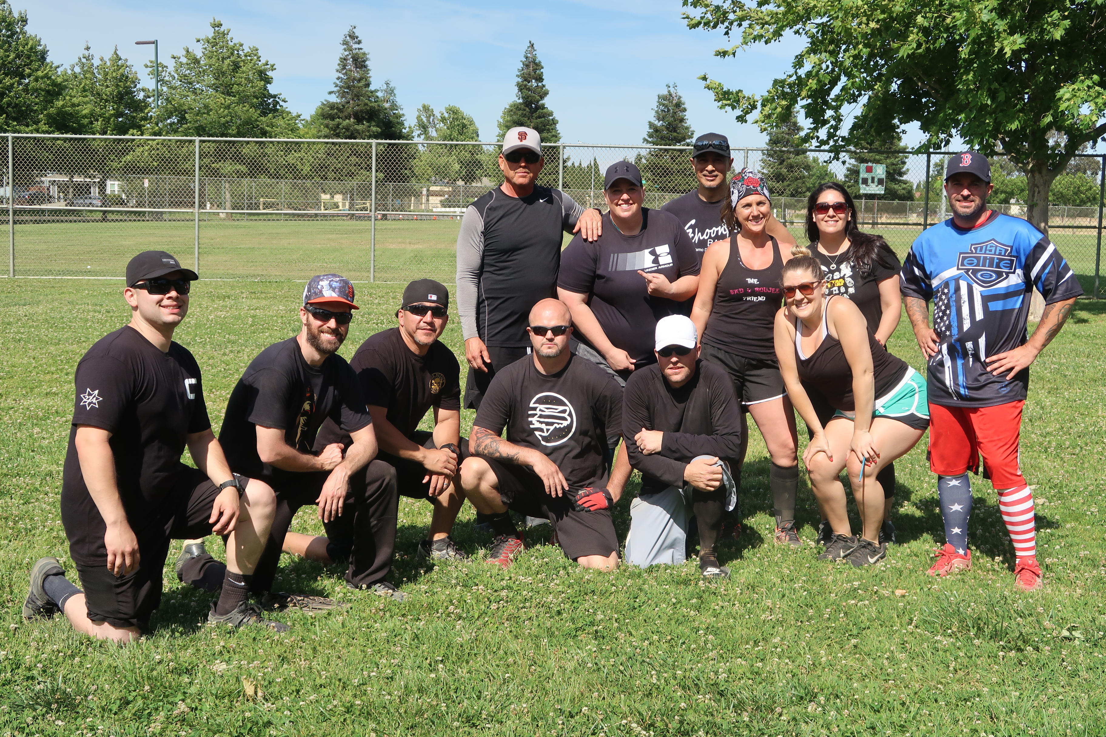 Men and women in softball uniforms pose on the grass.