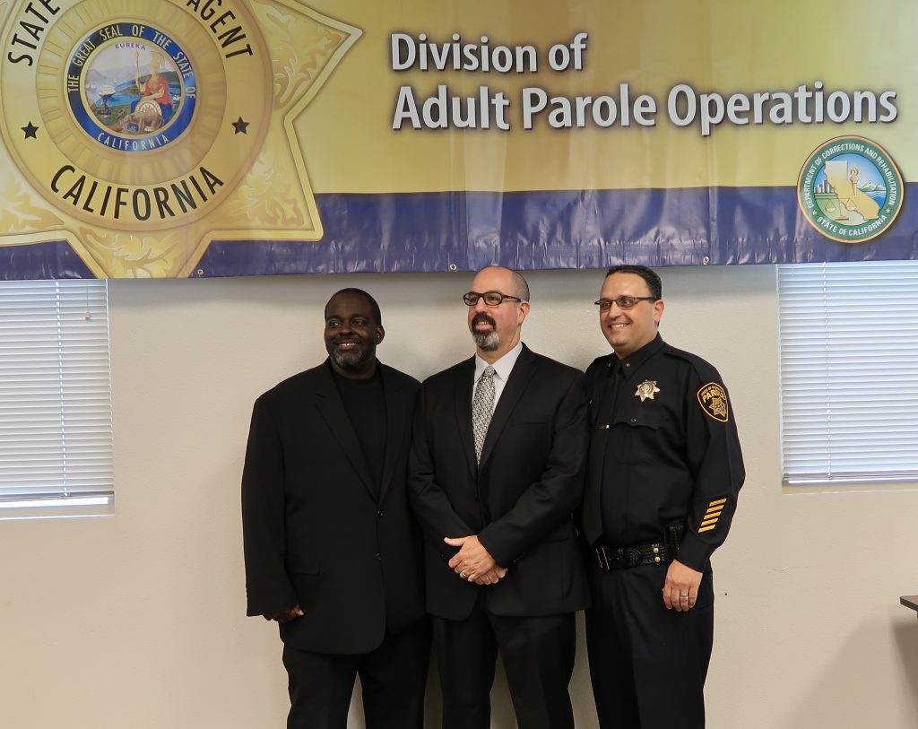 Three men stand in front of a banner that says Division of Adult Parole Operations.