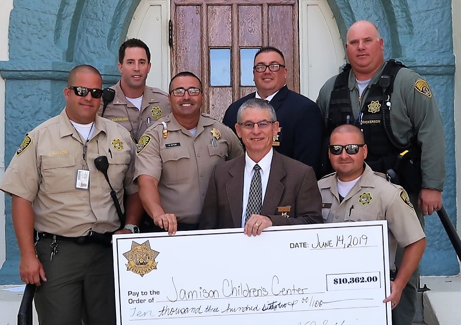 Five men in uniforms and two in suits hold a giant check from a golf tournament held by CCI.
