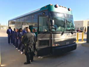 Prisoners getting on bus while correctional officer watches.