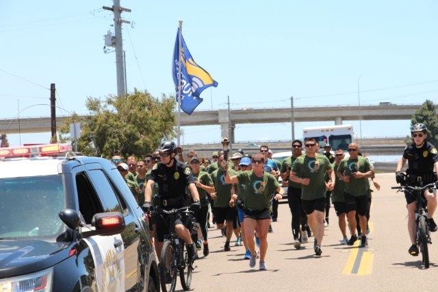 A police car and officers on bicycles escort runners carrying the Special Olympics torch.
