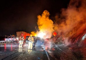 Smoke and flames with firefighters on a dark street.