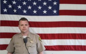 Man in uniform stands in front of U.S. flag.