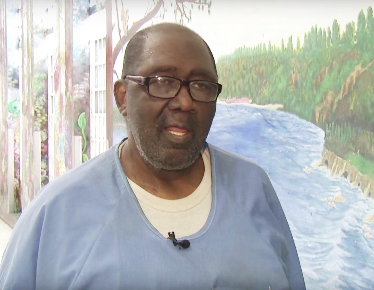 Man in blue shirt stands in front of nature mural at prison.