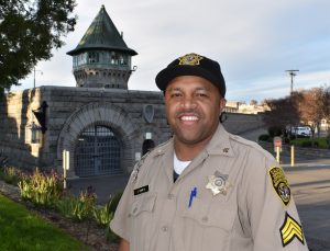 Uniformed man stands in front of gothic stone wall and tower.