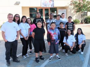Kids and adults smile outside a building with a banner that reads "Camp Suzanne."