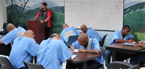 Men in blue clothing hunch over tables to write.