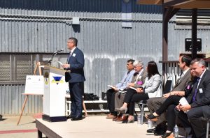 Man at podium speaks while others side on stage behind him.