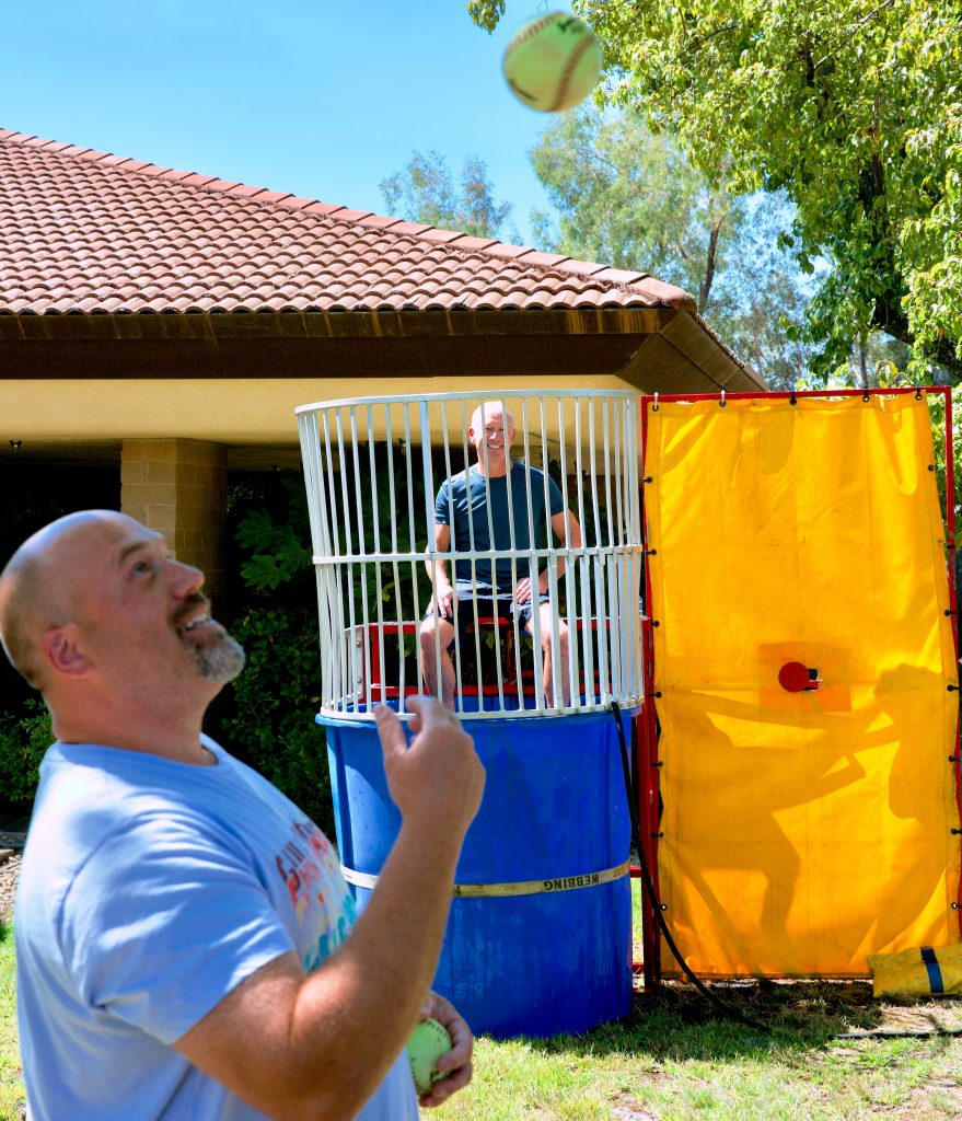 Man tosses ball in air as man in a dunk tank in the background looks on