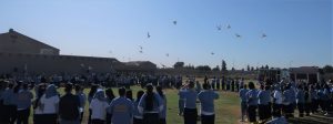 Birds fly over a women's prison while inmates look up to watch them.