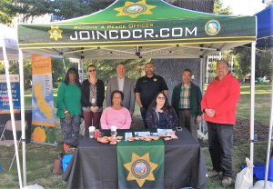 People stand under a shade cover that has the CDCR logo and the words JoinCDCR.com.