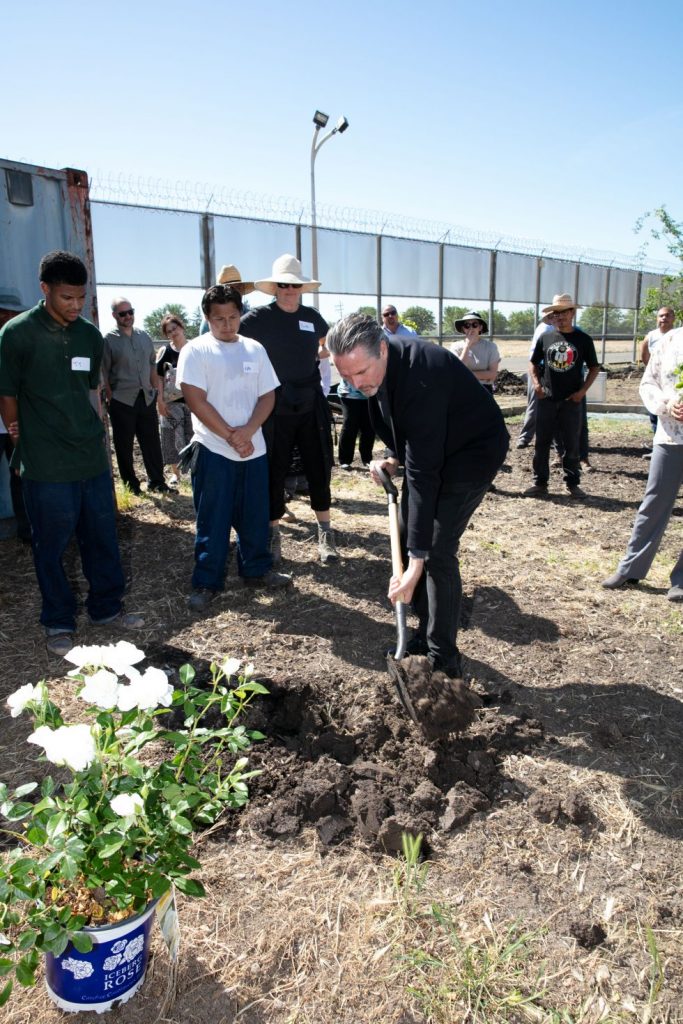 Man in suit shovels dirt while young offenders watch.