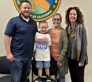 Three adults facing the camera and a small standing on a chair.