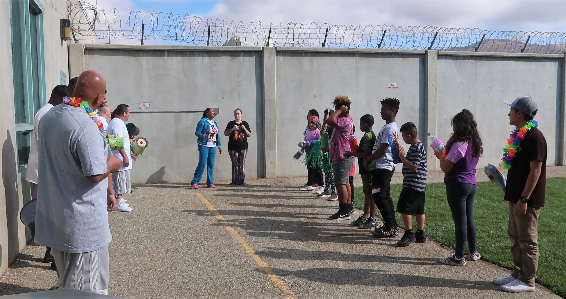 Children on the right and inmate fathers on the left stand in front of prison walls