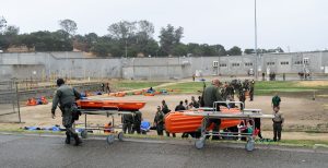 Officers and medical staff push gurneys in a prison yard.