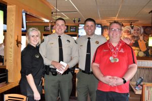 Two men in uniform are flanked by a restaurant server and a man wearing Special Olympics medals.