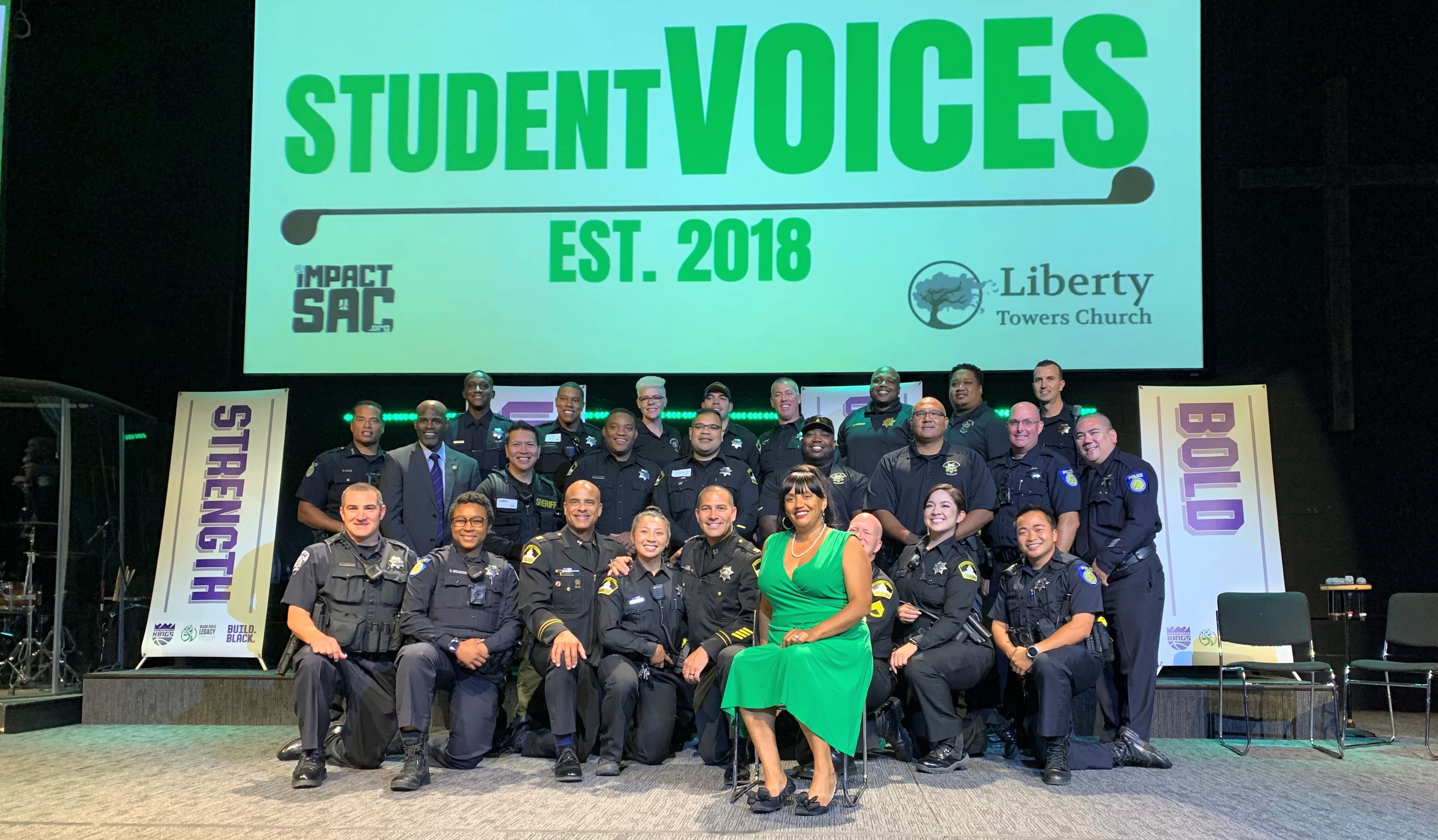 Men and women in uniform sit on a stage under the words Student Voices Est. 2018.