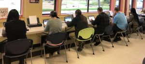 Six people sitting at computers with backs to camera