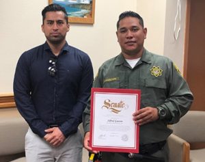 Man presents certificate to another man wearing a correctional officer's uniform.
