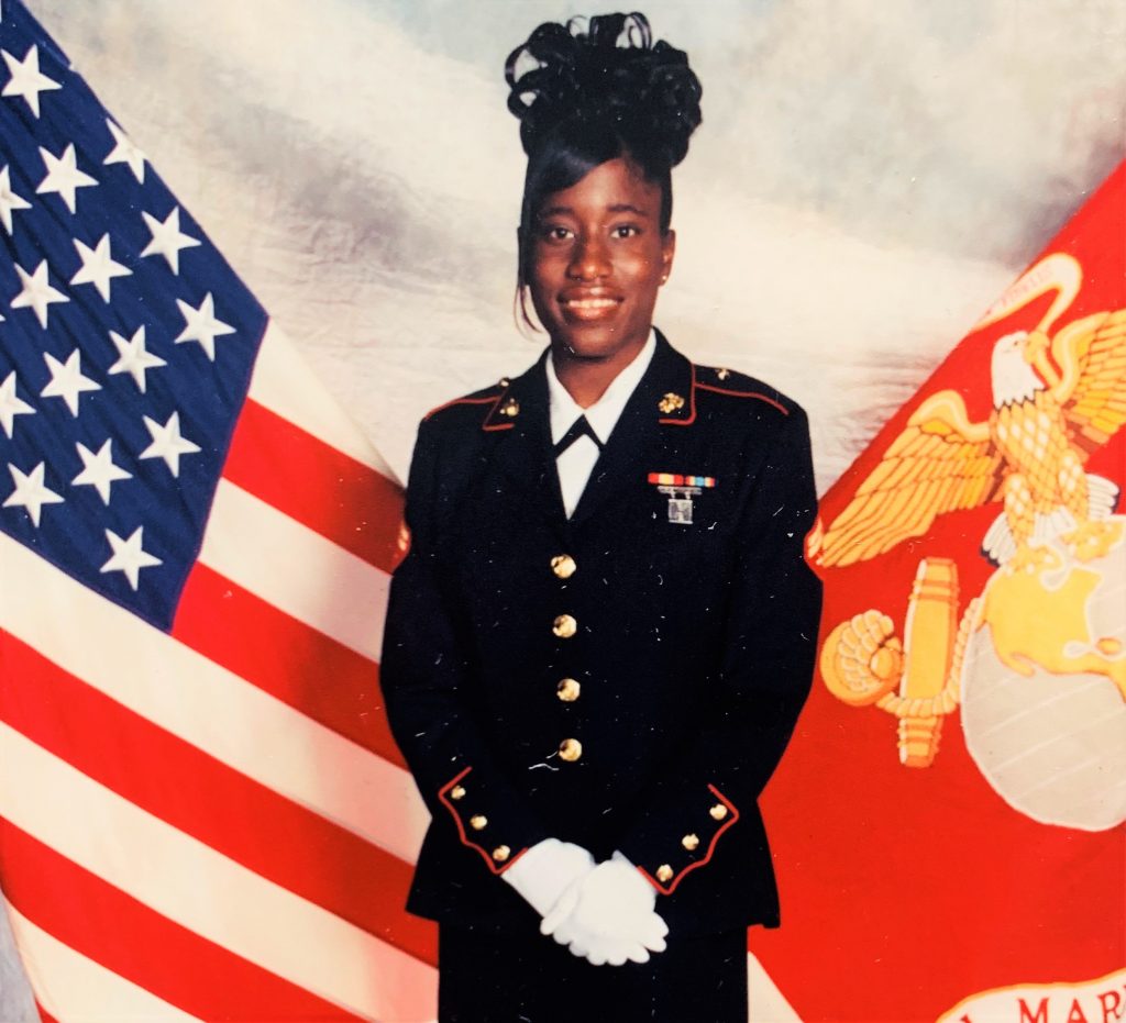 Woman in uniform in front of U.S. flag and Marine Corps flag.