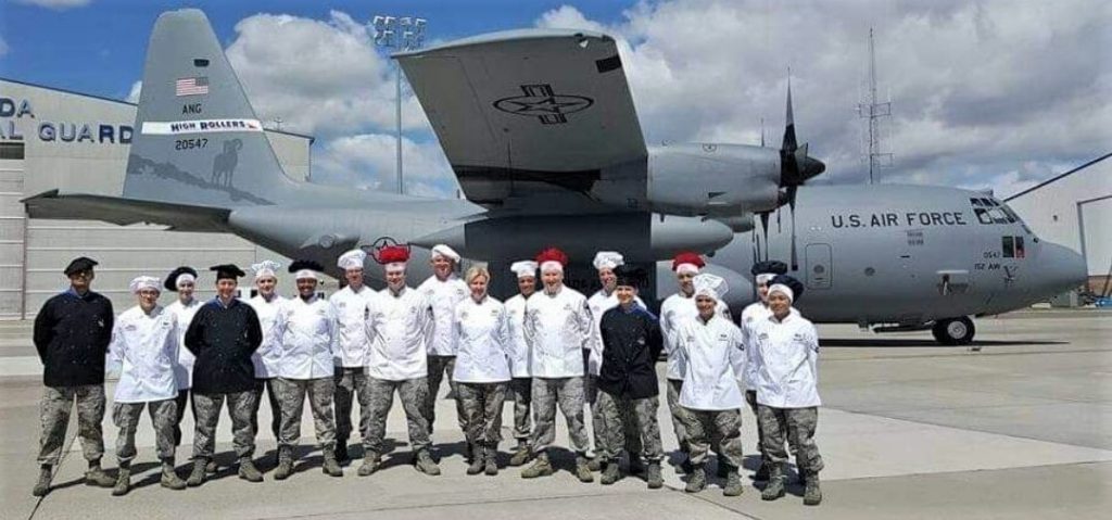 People wearing chef coats while standing in front of a large military plane.