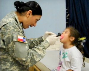 Woman in military uniform checks out a sick child.
