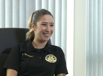 Smiling woman wears dark shirt with a badge logo on it and the name V. Melendez.
