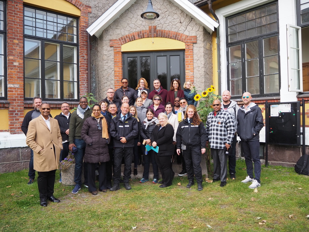 Correctional staff and leadership from California and Norway stand in front of a brick house.