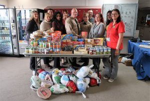 A pile of frozen turkeys is in front of a table full of food. Behind the table are two uniformed staff and others in civilian clothing.