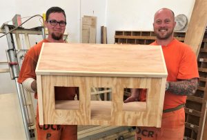 Two inmates hold a large dollhouse.