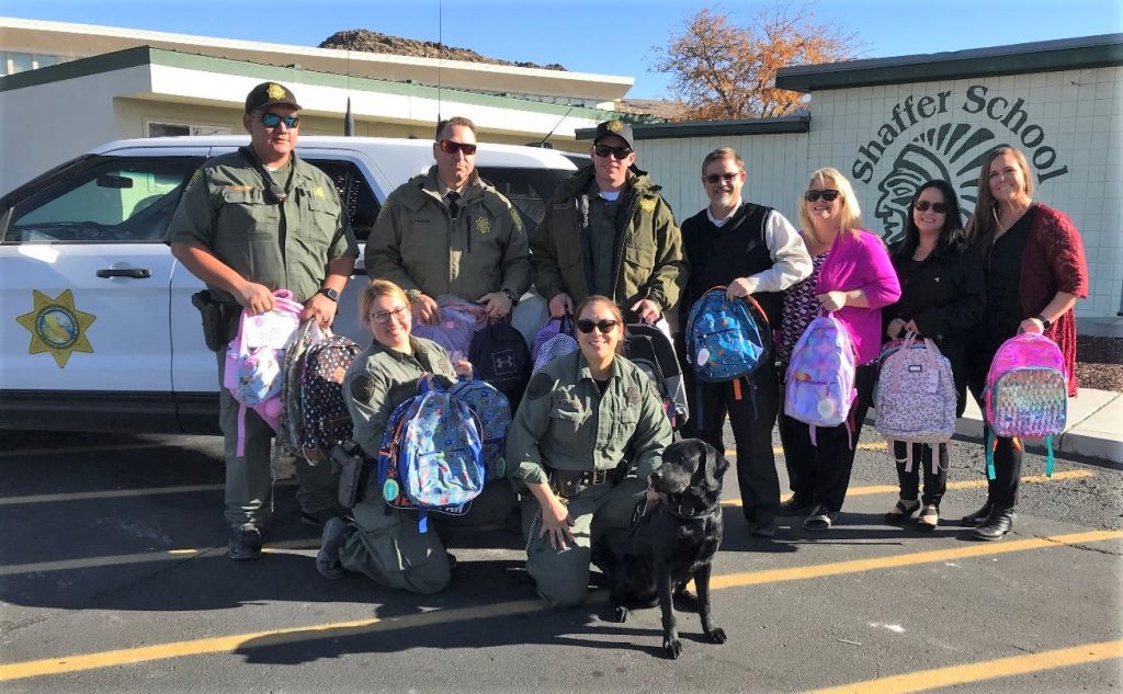 Uniformed officers and a dog deliver backpacks to a school.
