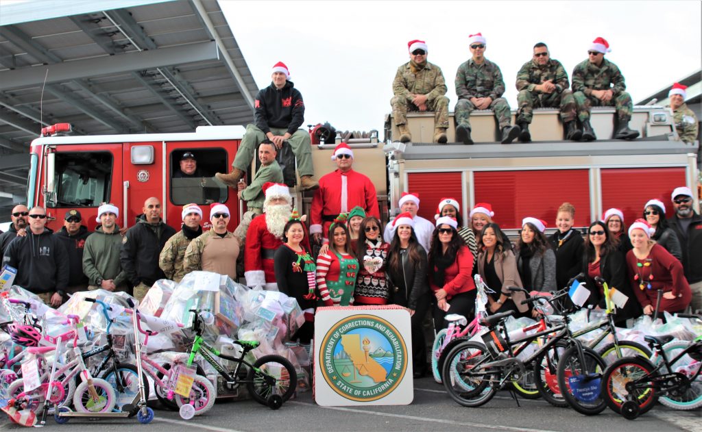 Officers and prison staff, along with Santa Claus, pose with a pile of toys and bicycles around a fire engine.