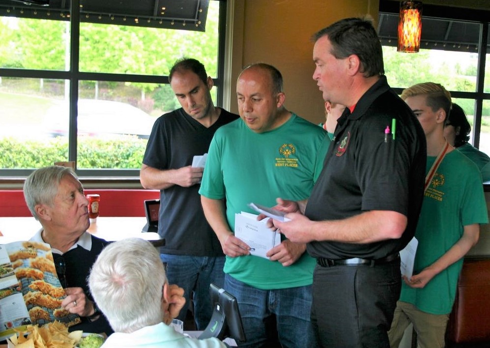 Man explains a fundraiser to two diners at Chili's restaurant while three Special Olympics athletes nearby.