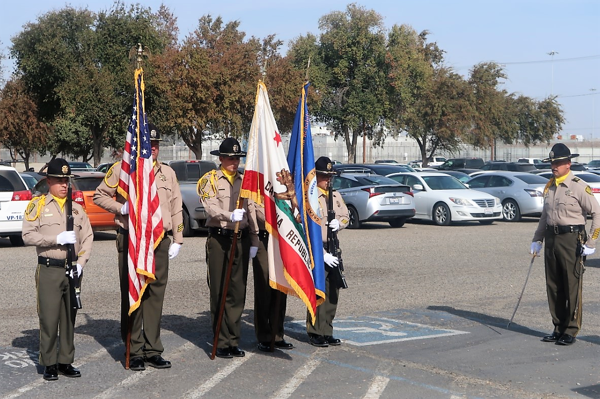 Correctional staff in uniform stand at attention while holding flags.