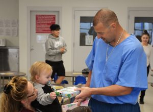 Inmate gives a gift to a toddler in a prison visiting room.