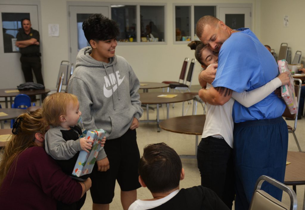 Girl hugs her incarcerated father while other families look on.