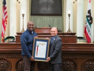 Two men hold a framed resolution while standing in the California state Capitol.
