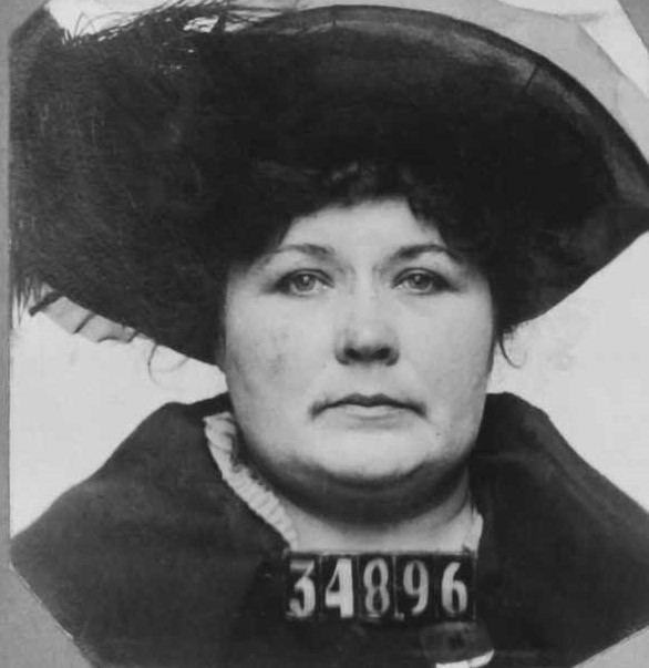 Woman wears a large hat with the numbers 34896 in her San Quentin mugshot.