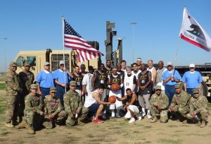 Soldiers and inmates stand in front of a large military vehicle.