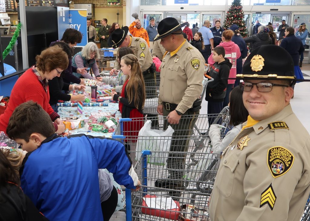 Three correctional staff stand with children while they get presents wrapped.